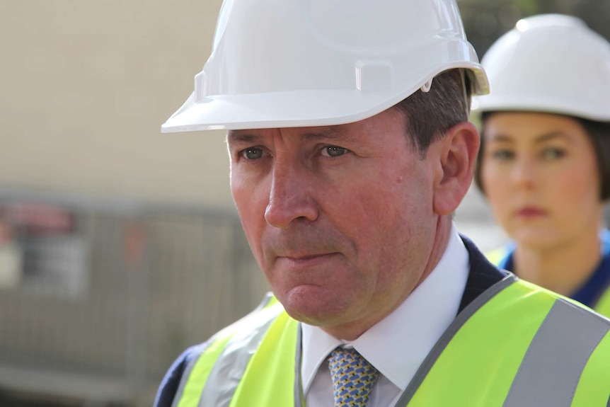 A tight head and shoulders shot of WA Premier Mark McGowan wearing a white hard hat and yellow hi vis vest.