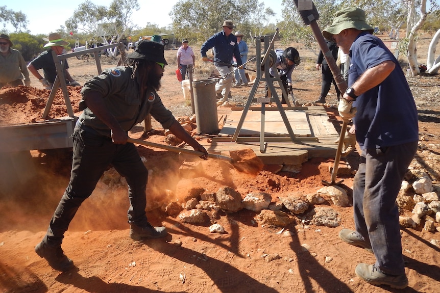 Two people dig red dirt near a well. 