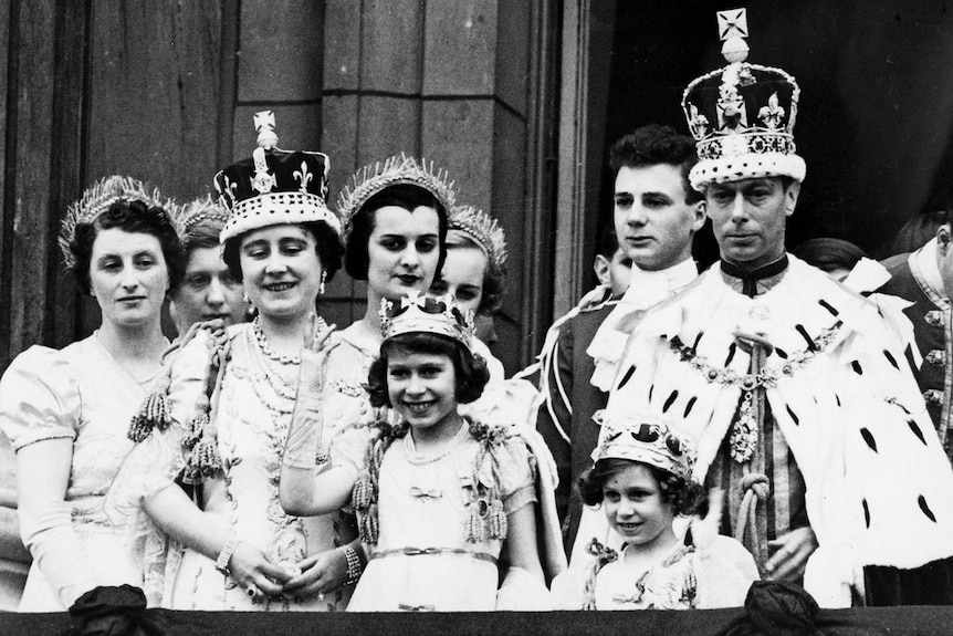 A black and white photo of Queen Elizabeth and her sister as children waving from a balcony with their parents behind them