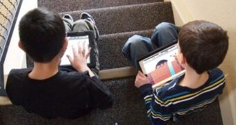 Children sit on steps with ipads.