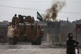 Syrian opposition fighters on an armoured personnel carrier in front of smoke
