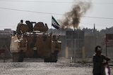 Syrian opposition fighters on an armoured personnel carrier in front of smoke