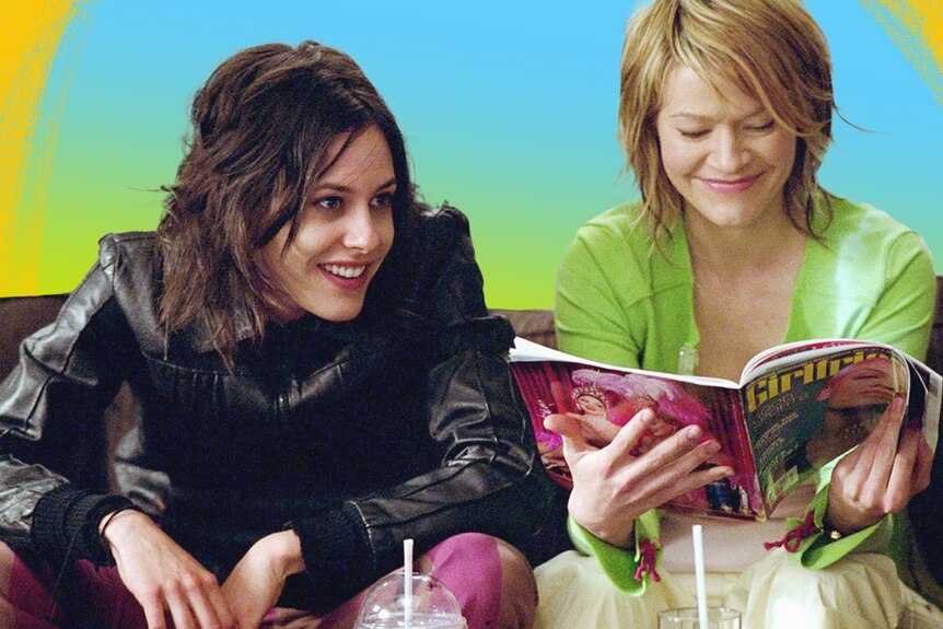 The L Word's Shane and Alice smile on a couch - Alice reads Girlfriend magazine.