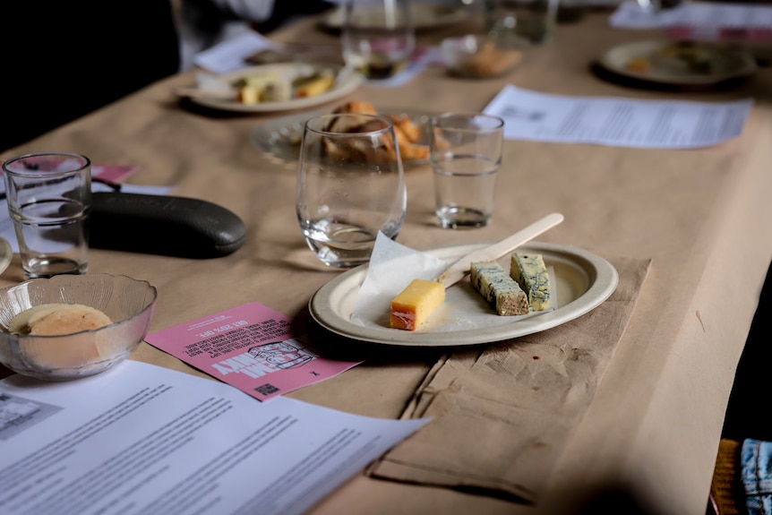 A plate of three cheeses sits on a long table amid glasses of water and menus 