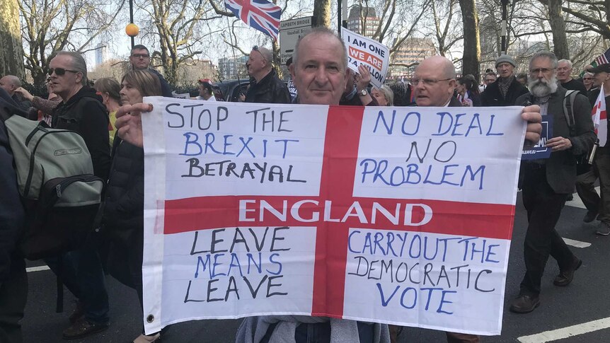 Man holds up pro-Brexit sign, as dozens of other protesters march in the street behind him