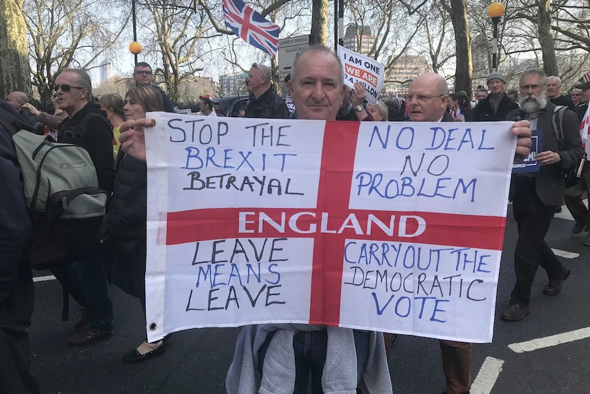 Man holds up pro-Brexit sign, as dozens of other protesters march in the street behind him
