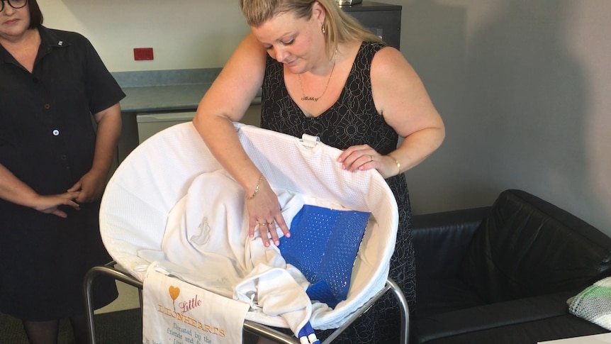 A woman standing behind a bassinet pulls open the sheets