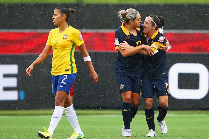 Soccer players hug each other in the rain while another walks away after a goal