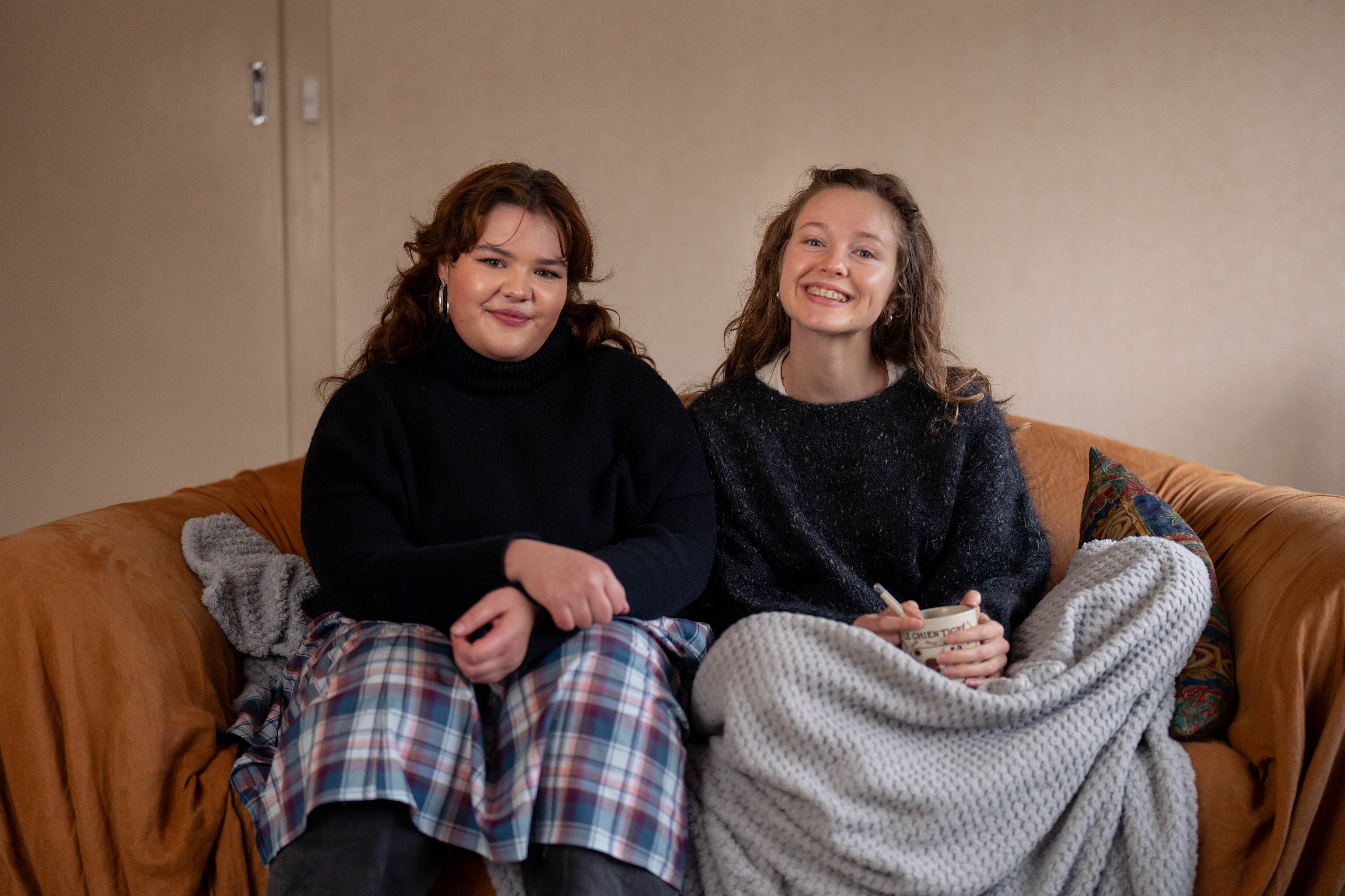 Two girls sit on a couch and smile for a photo