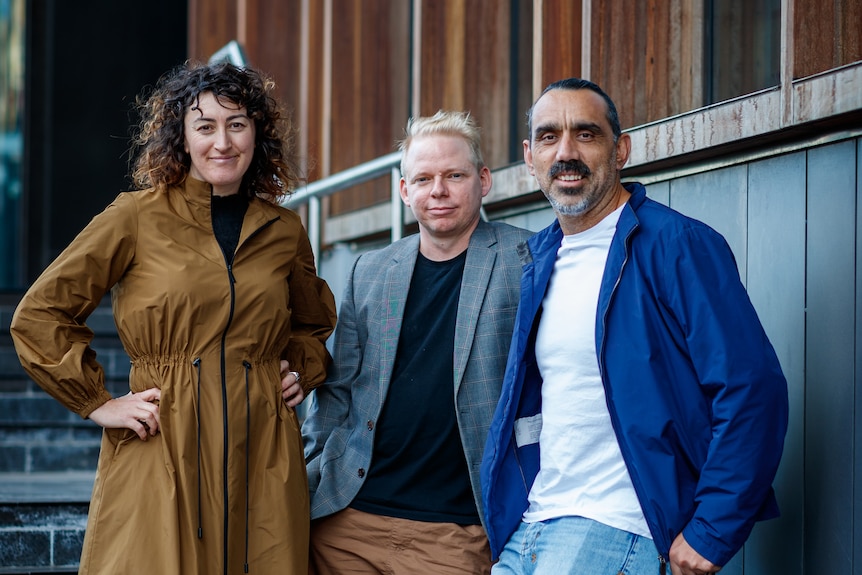 Professor Angie Abdilla, Dr Baden Pailthorpe and Adam Goodes pose for a photo on some steps.