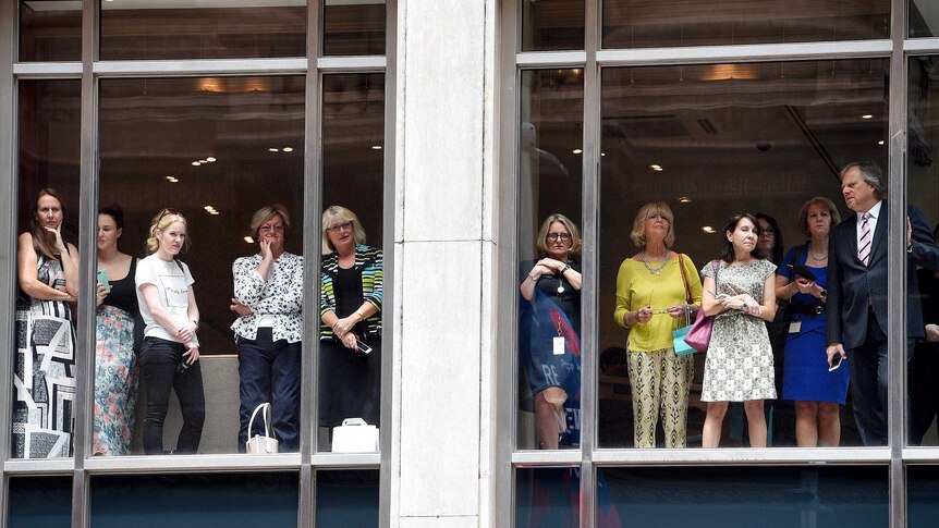 Office workers look out from a building as they watch Prince Charles and the Duchess of Cornwall meet with members of the public