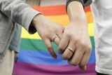 Two women hold hands in front of a rainbow flag