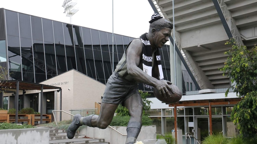 Floral tributes and a Magpies scarf are placed on a Lou Richards statue outside Collingwood Football Club.