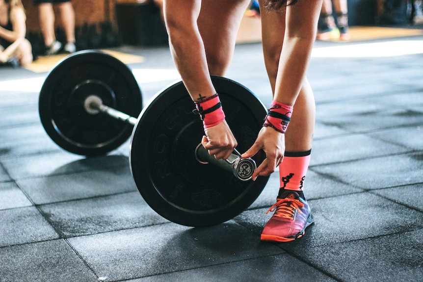 Woman at gym getting ready to pick up a heavy weight for a story about not using towels to wipe down gym equipment.