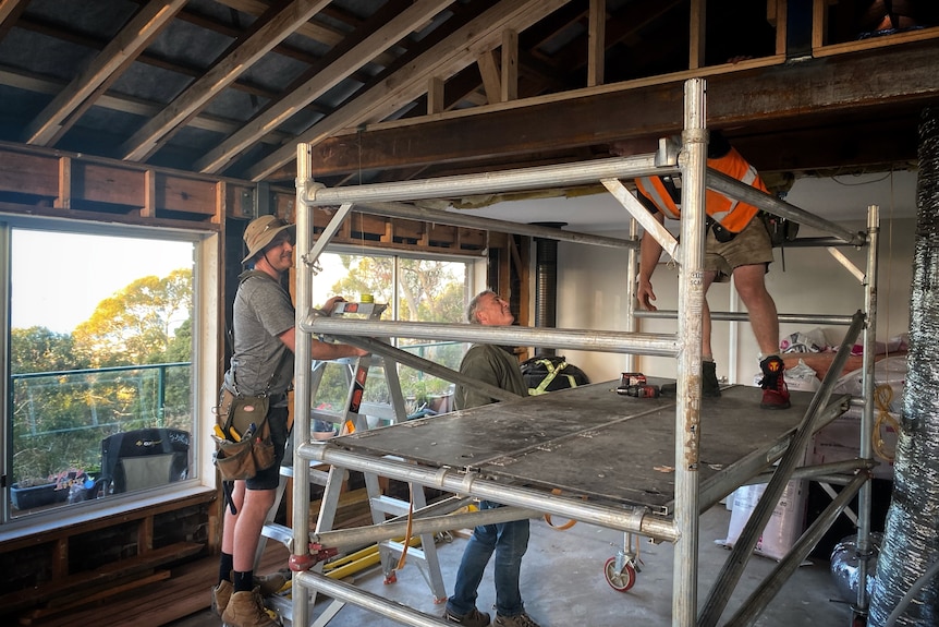 Three builders inside a house that is under construction.