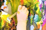 A child's hand holds a pain brush and paints a picture.