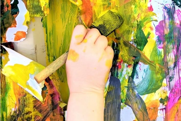 A child's hand holds a pain brush and paints a picture.