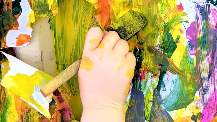 A child's hand holds a pain brush and paints a picture.