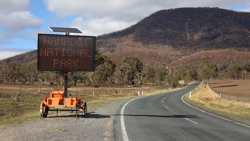 A sign at the front of Namadgi National Park with burnt forest in the distance