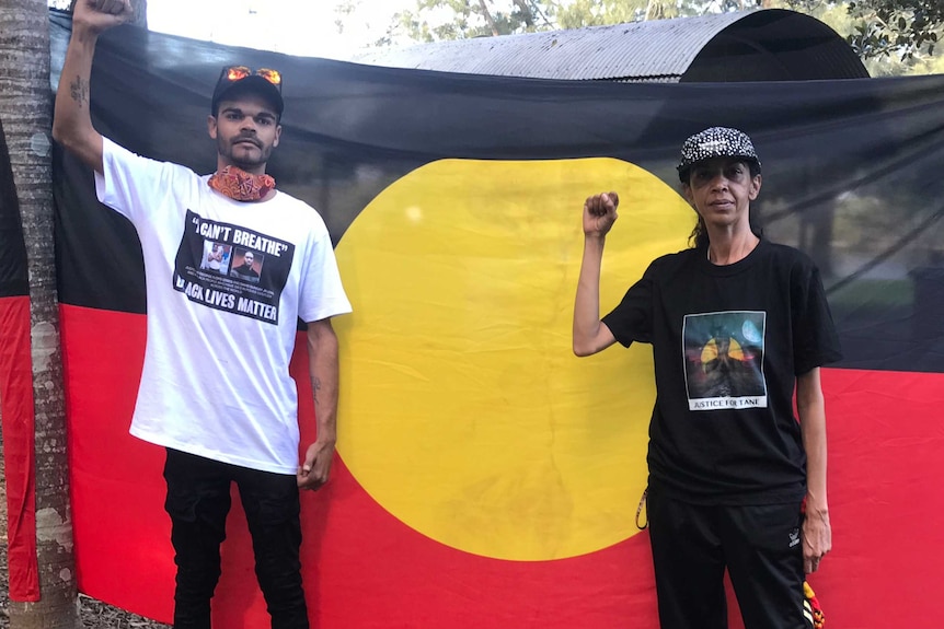 Two people stand in front of an Aboriginal flag.