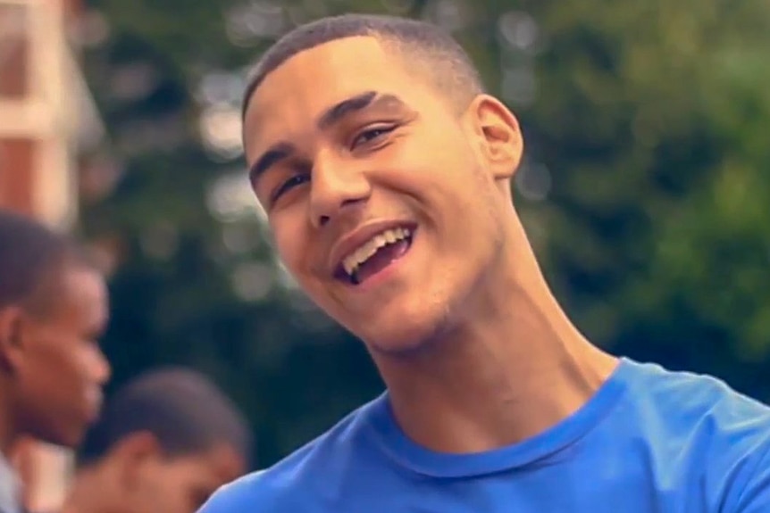 Rapper Joshua Ribera, wearing a blue T-shirt and smiling at the camera