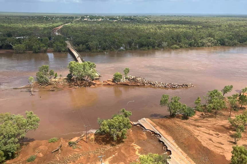 A destroyed bridge sits amongst a bulging brown river