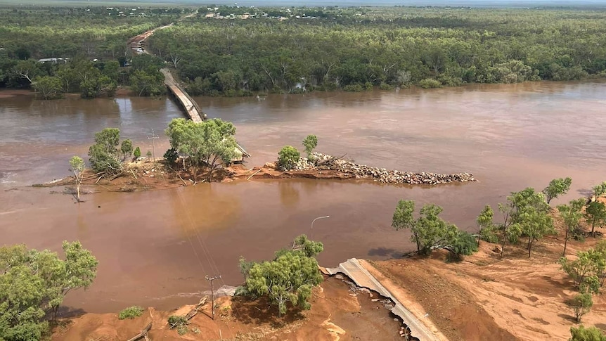 A destroyed bridge sits amongst a bulging brown river