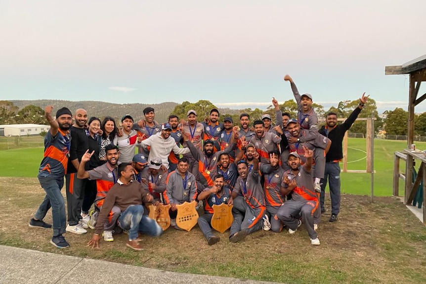 A group of men standing together, wearing team colours, with three sport shields being held by those in the front row