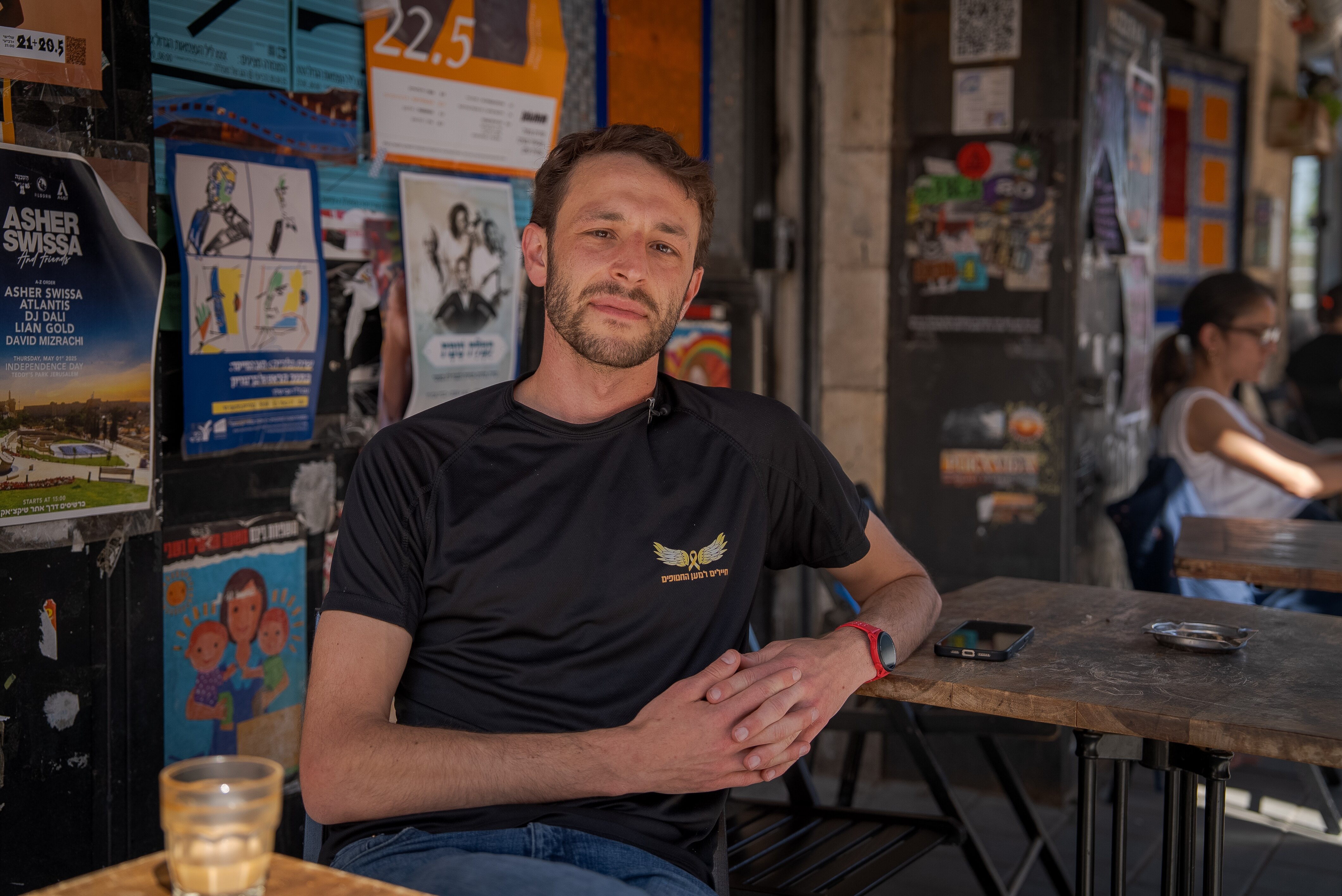 Max Kresch sits in the shade outdoors at a table with an empty glass in front of him.