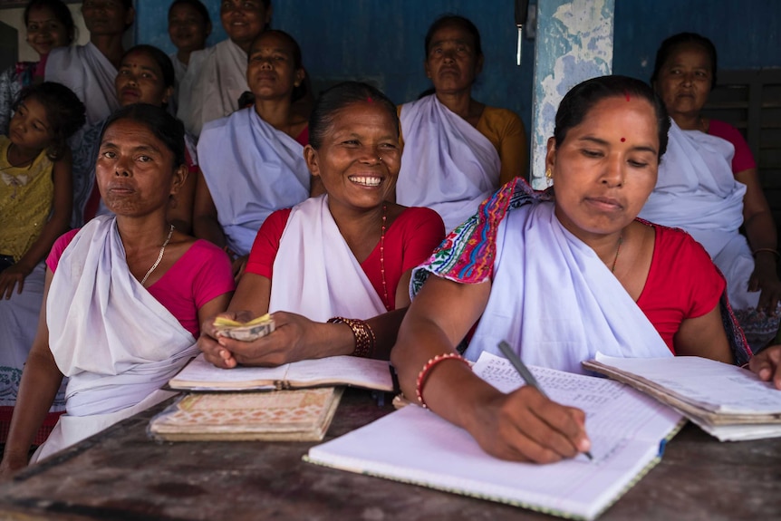 Nepalese women write in books and handle money at a desk.