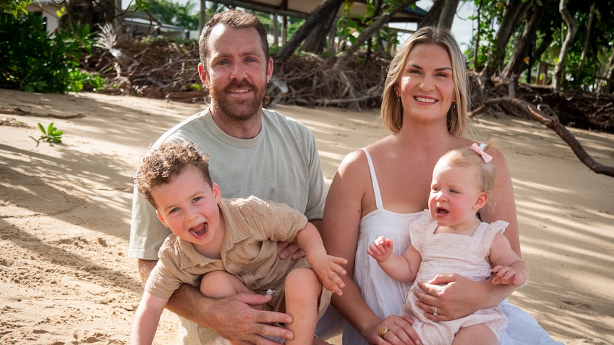 father adrian with wife nicole and young children leonardo and luna sit on the sand at a beach