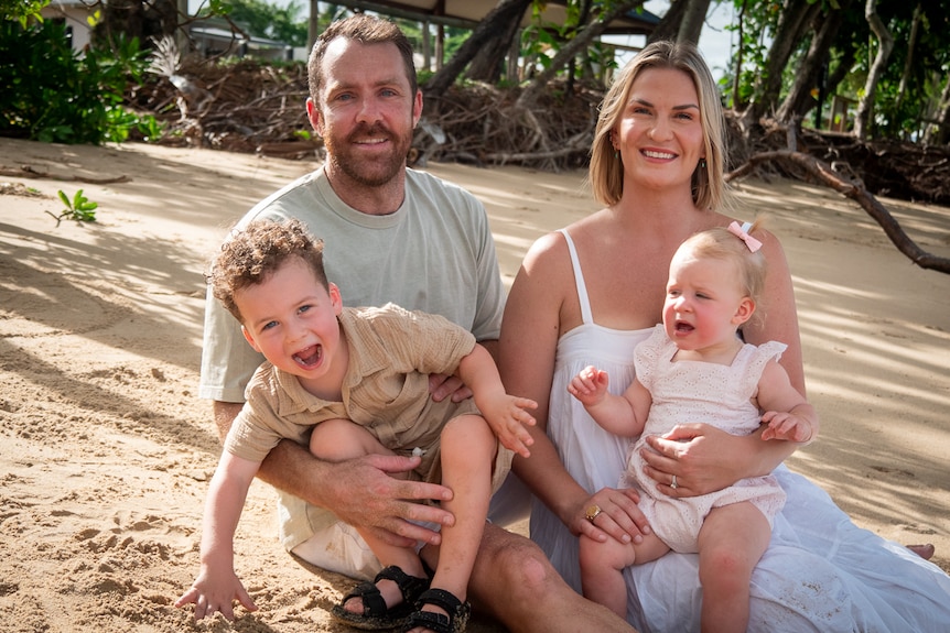 father adrian with wife nicole and young children leonardo and luna sit on the sand at a beach