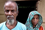 A man wearing a blue shirt stands next to a woman wearing a turquoise hijab.