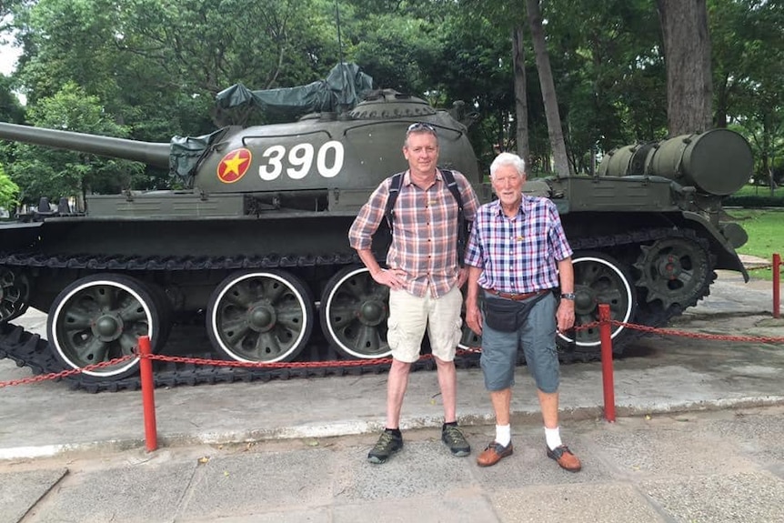 Two men standing in front of tank with Vietnam emblem on it