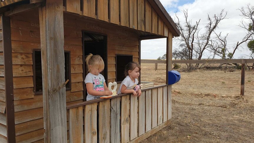 Two young girls stand inside a small wooden house