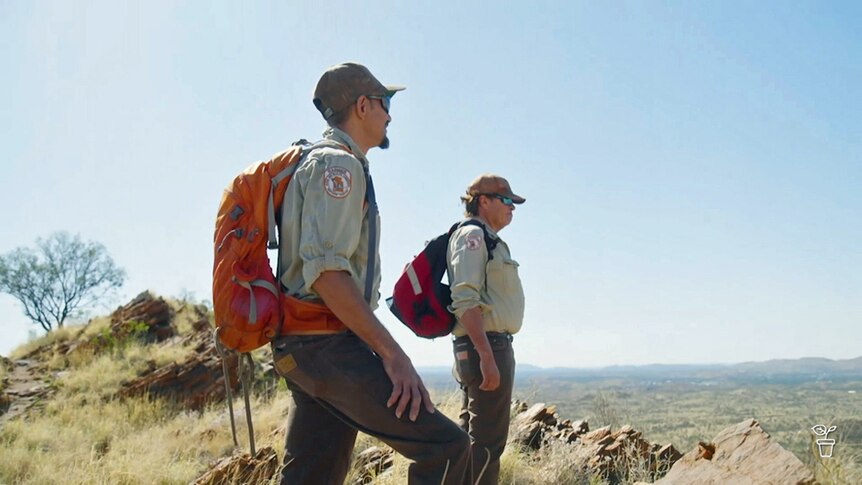 Two Rangers with backpacks standing looking out over desert country.