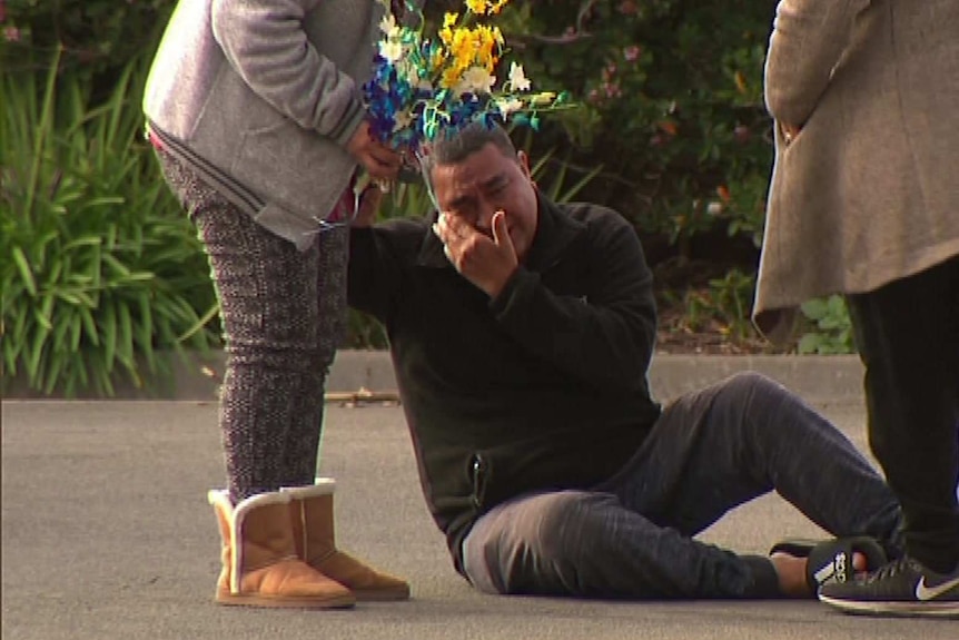 A man sits on the ground, crying.