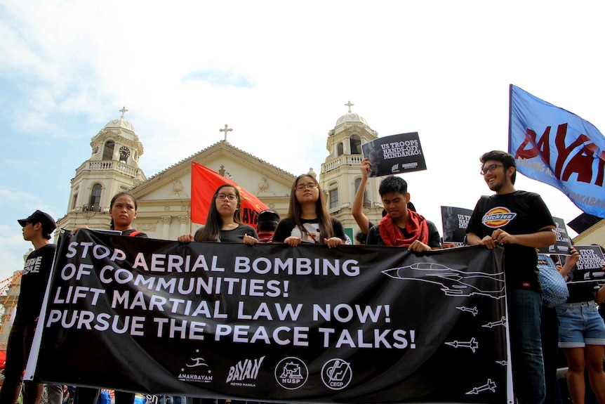 A group of protestors hold up a sign saying "Stop aerial bombing our communities! List martial law now! Pursue Peace the talks."