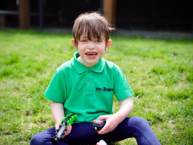 A little boy sitting in the grass smiling