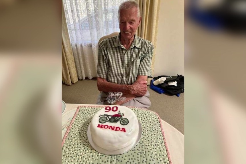 An elderly man looks at a birthday cake.