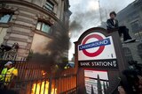 A G20 protester looks on as a fire burns near the entrance to Bank Tube station