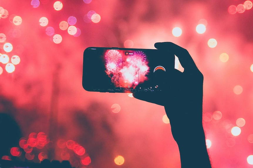 A person holds up their mobile phone to record fireworks in front of them.
