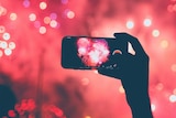 A person holds up their mobile phone to record fireworks in front of them.