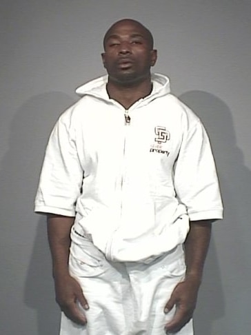 A Nigerian man stands for a mug shot wearing a full white tracksuit. He is visible from the waist up.