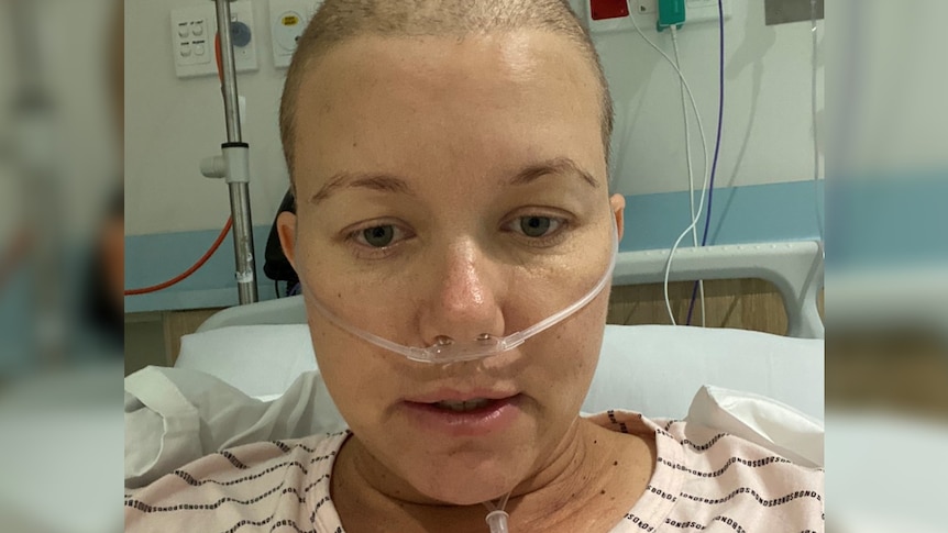 A woman with a shaved head and nose tube in hospital bed