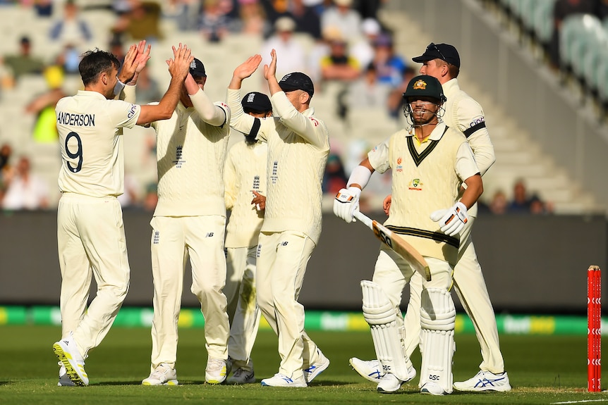 A cricket bowler high fives with his teammates after dismissing a batsman who walks off lifting his bat up