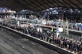 Crowds of people wait on a platform for trains at Southern Cross Station in Melbourne.