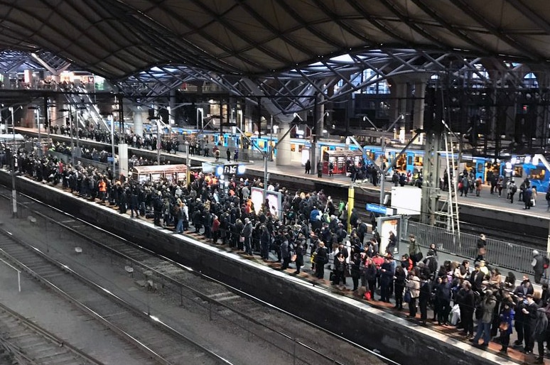 Crowds of people wait on a platform for trains at Southern Cross Station in Melbourne.