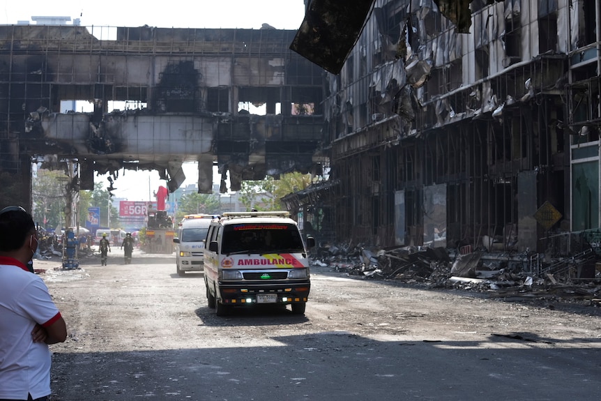 Ambulances drive along a road that runs through the wrecakge of a burned large hotel.