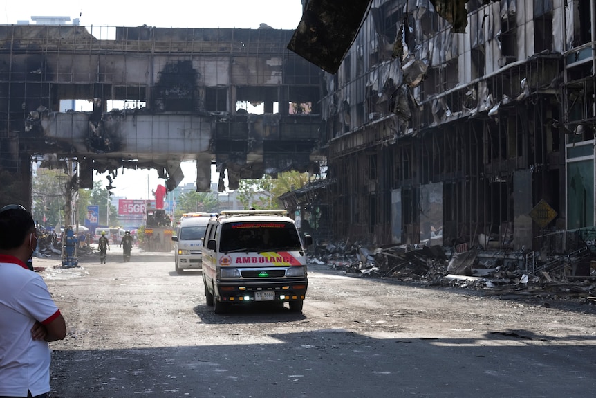 Ambulances drive along a road that runs through the wrecakge of a burned large hotel.